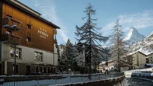 Un hotel con fachada de madera, un restaurante y vistas a árboles y montañas nevadas.