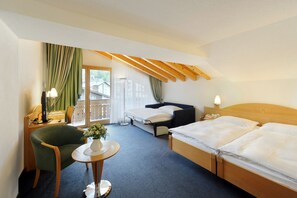 A hotel room with a bed, a desk with a computer, a chair, a small table with a vase, and a balcony with curtains. - Alpine Hotel Perren (Zermatt)