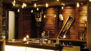 Zona de bar rústica con paredes de madera, vigas a la vista y lámparas colgantes.
