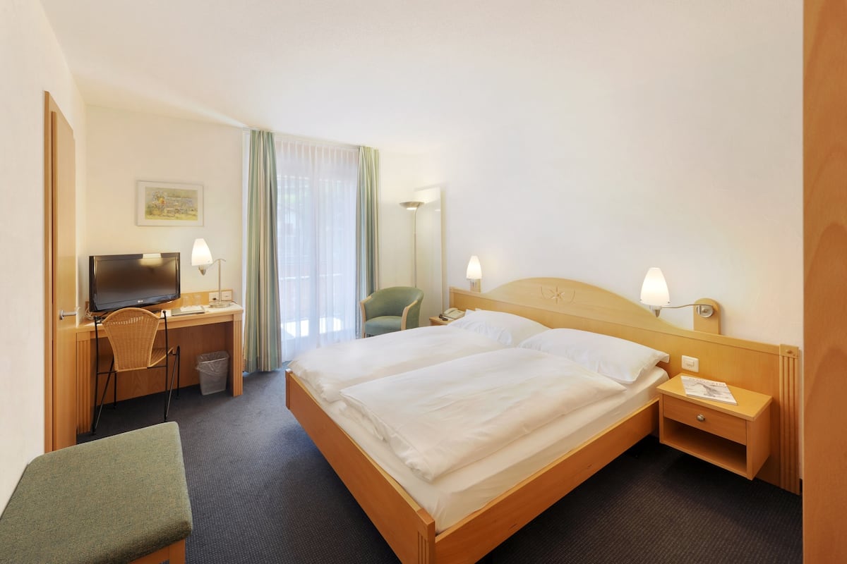 A hotel room with a bed, desk, chair, and a television.