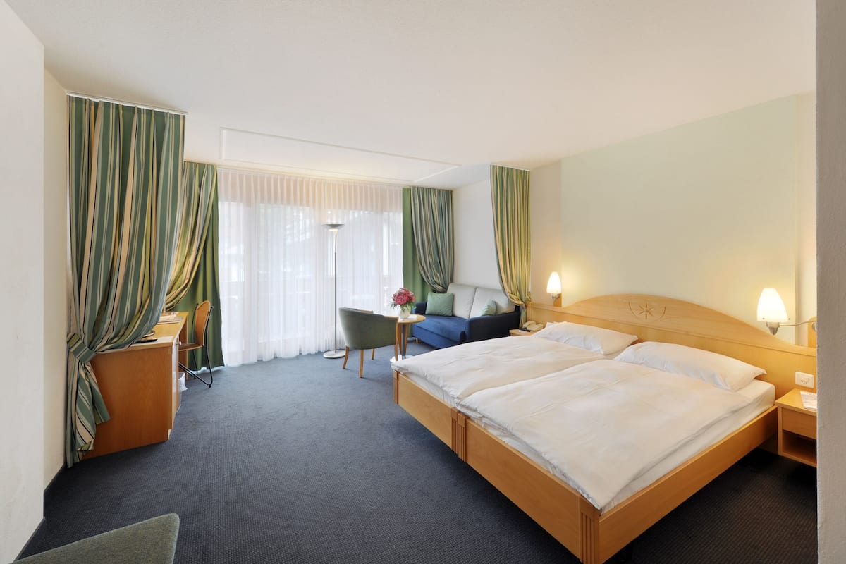 A hotel room with a double bed, a desk, a chair, a sofa, and curtains.