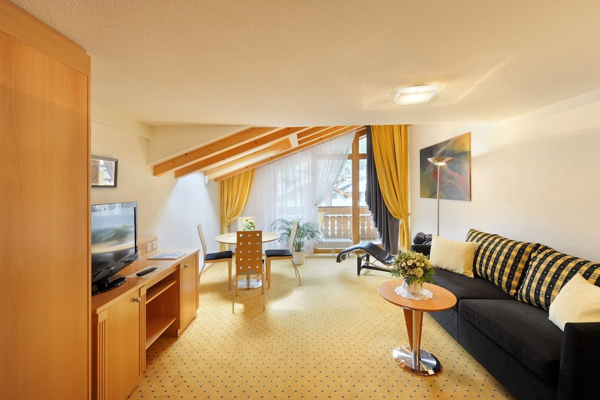 A modern living room with a sofa, a TV, a dining table with chairs, and a balcony with yellow curtains.