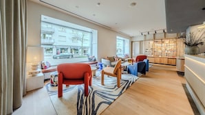 A modern living room with a large window, a sofa, a chair, and a small table. - Sorell Boutique-Hotel Seefeld Zürich (Zürich)