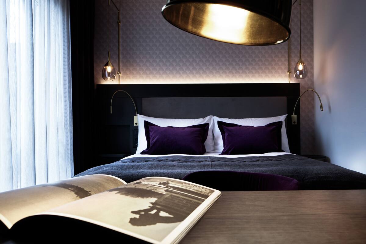 A neatly made bed with a dark headboard, two bedside lamps, and an open book on the nightstand.