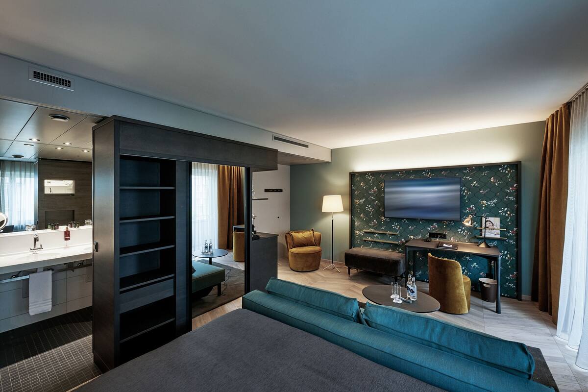 A modern hotel room with a large bed, a sofa, a desk, and a TV.