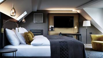 A modern hotel room with a bed, bedside table, lamp, and a TV mounted on the wall.