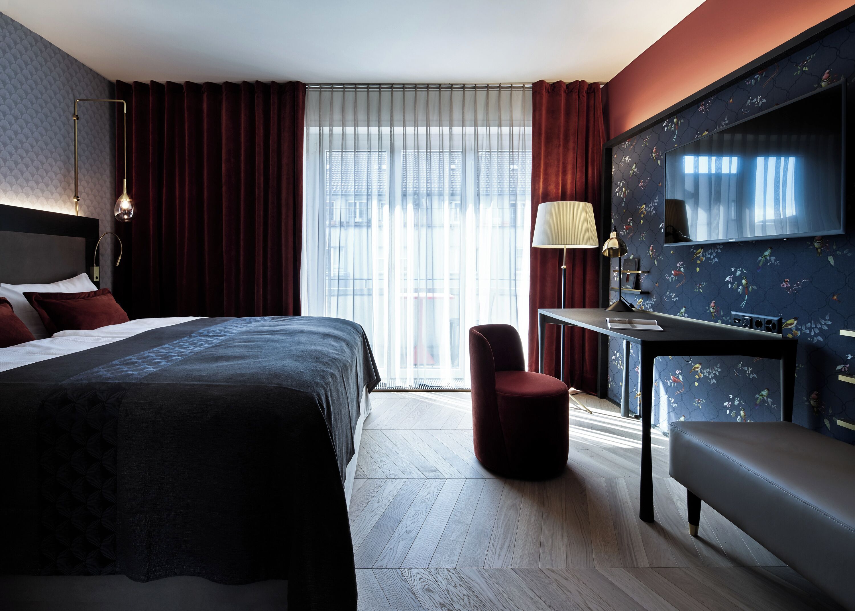 A modern hotel room with a large bed, a desk, a chair, and a sofa.