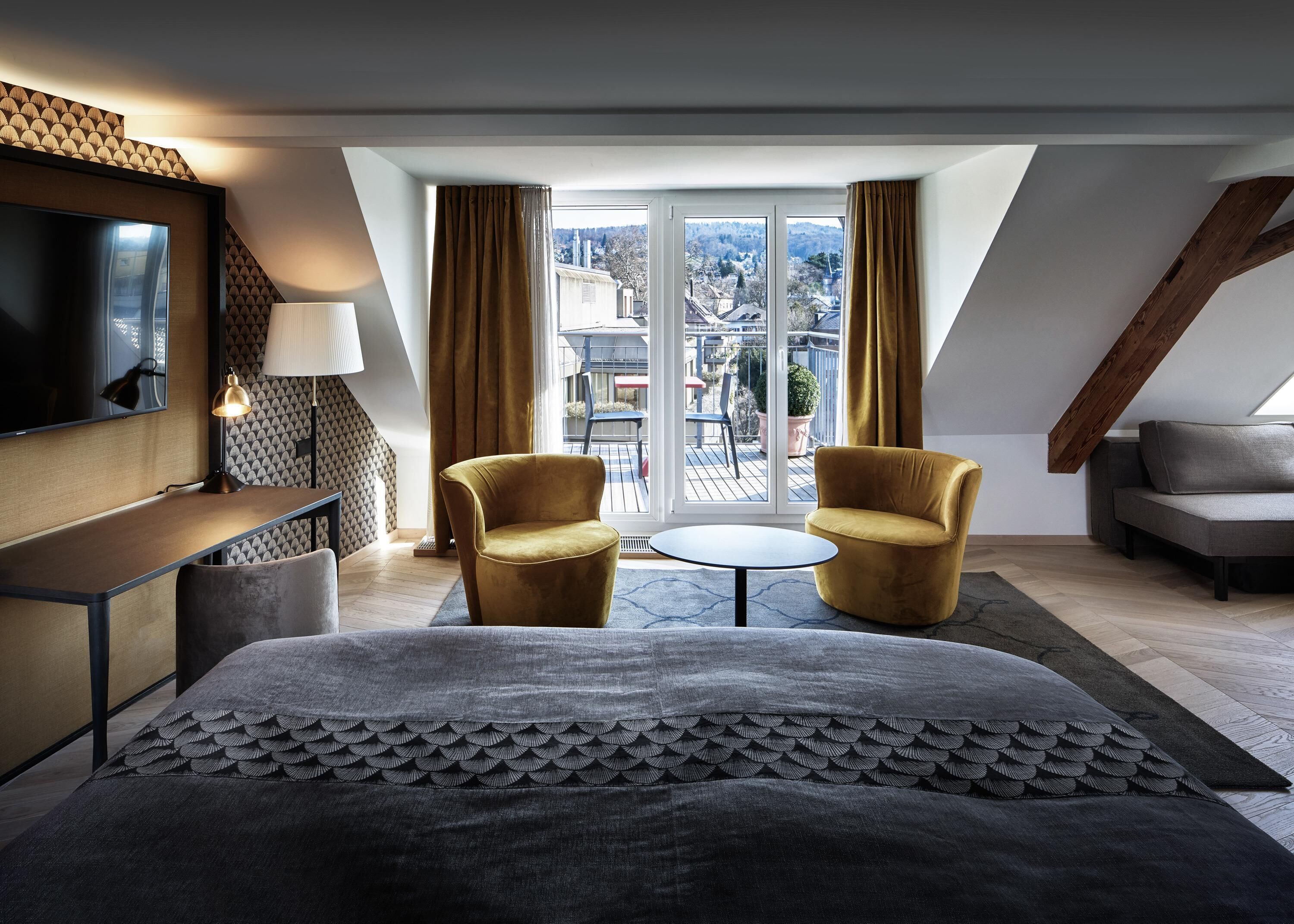 Ein modernes Hotelzimmer mit einem Bett, zwei Sesseln, einem kleinen Tisch, einem Fernseher und einem Balkon mit Aussicht.
