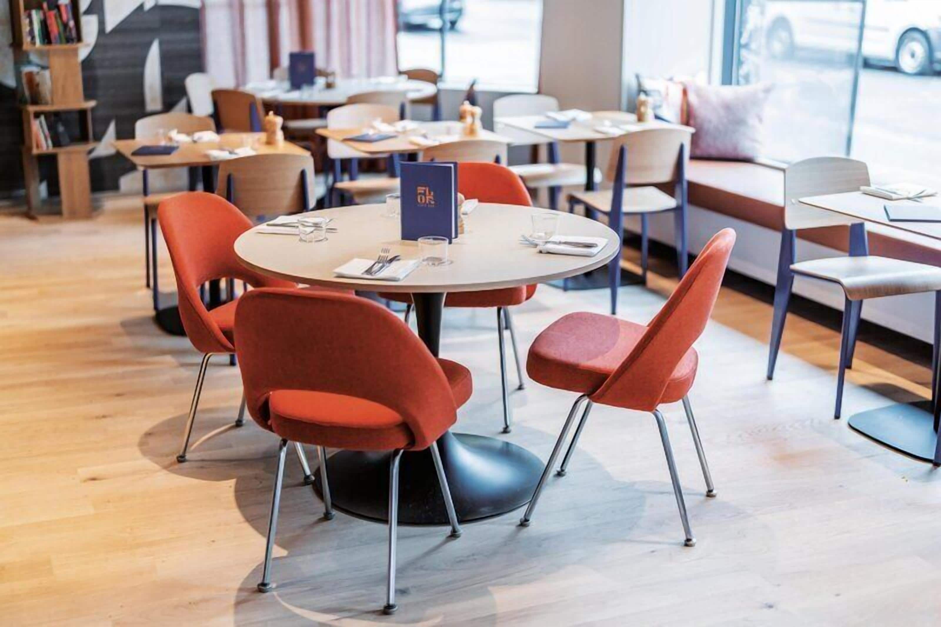 A restaurant with round tables, red chairs, and a blue menu stand.