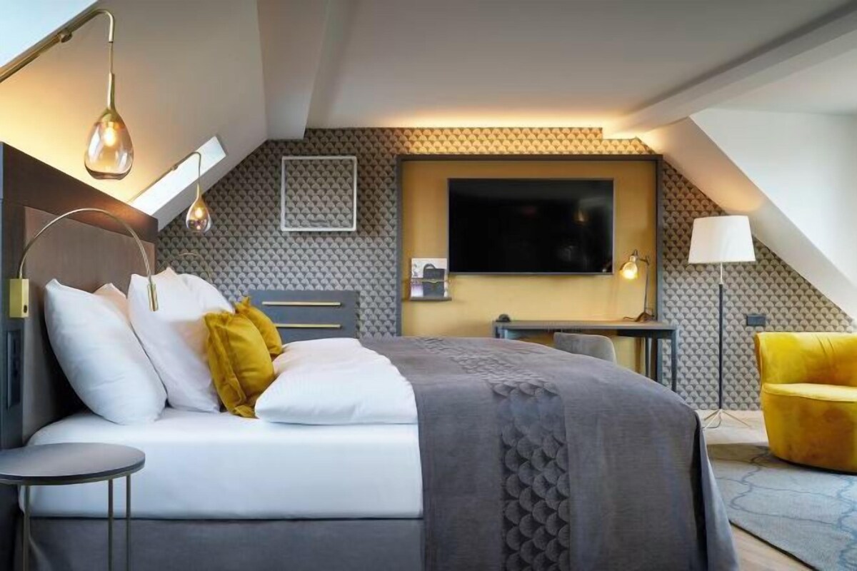 A modern hotel room with a bed, bedside table, and a TV mounted on the wall.
