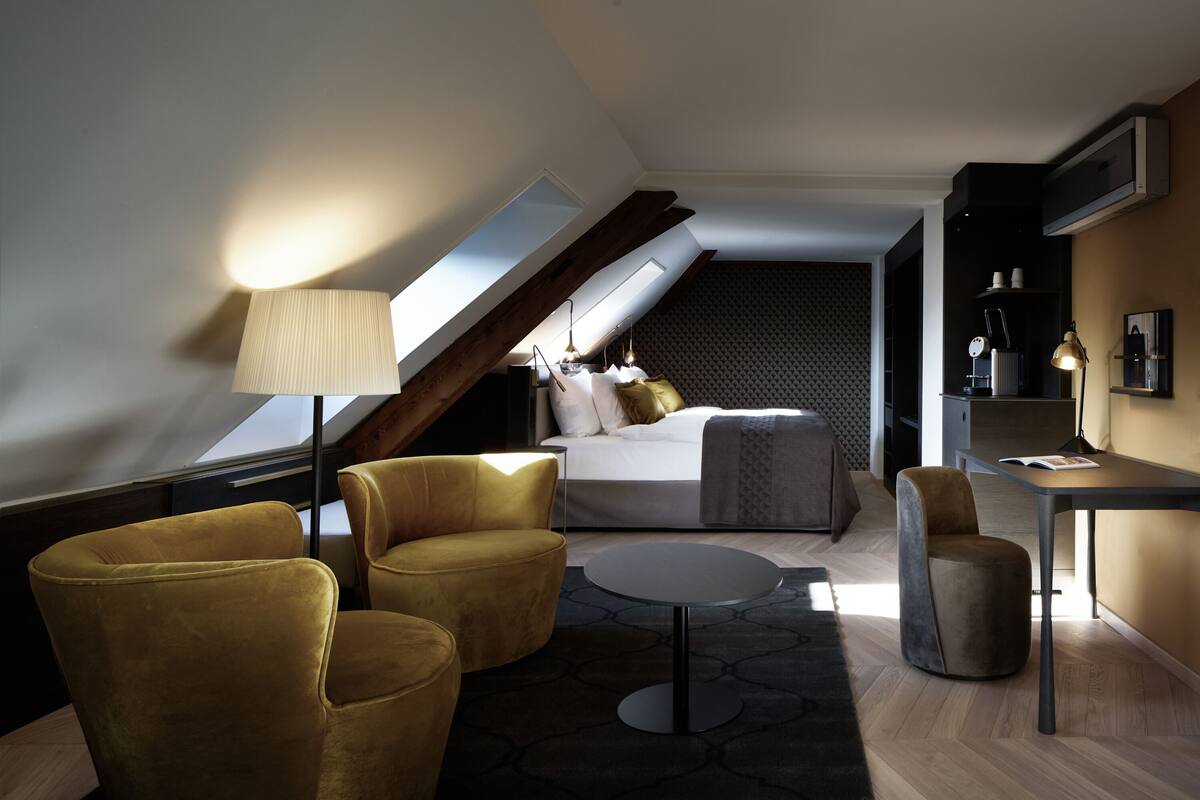 A modern loft bedroom with a skylight, a bed, a desk, and seating areas.
