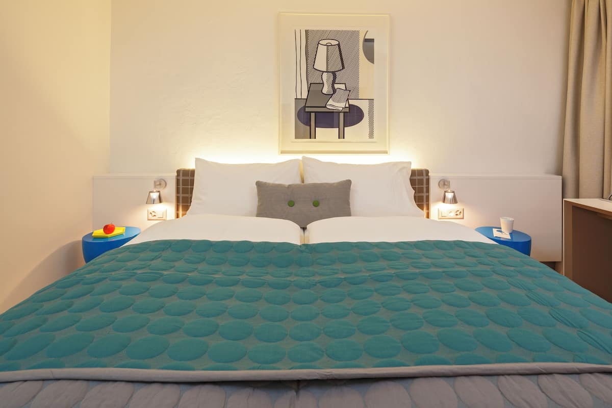 A neatly made bed with a teal quilt, two pillows, and bedside tables with lamps.