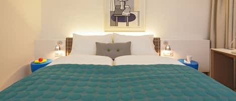 Una cama bien hecha con colcha color aguamarina, dos almohadas y mesitas de noche con lámparas.