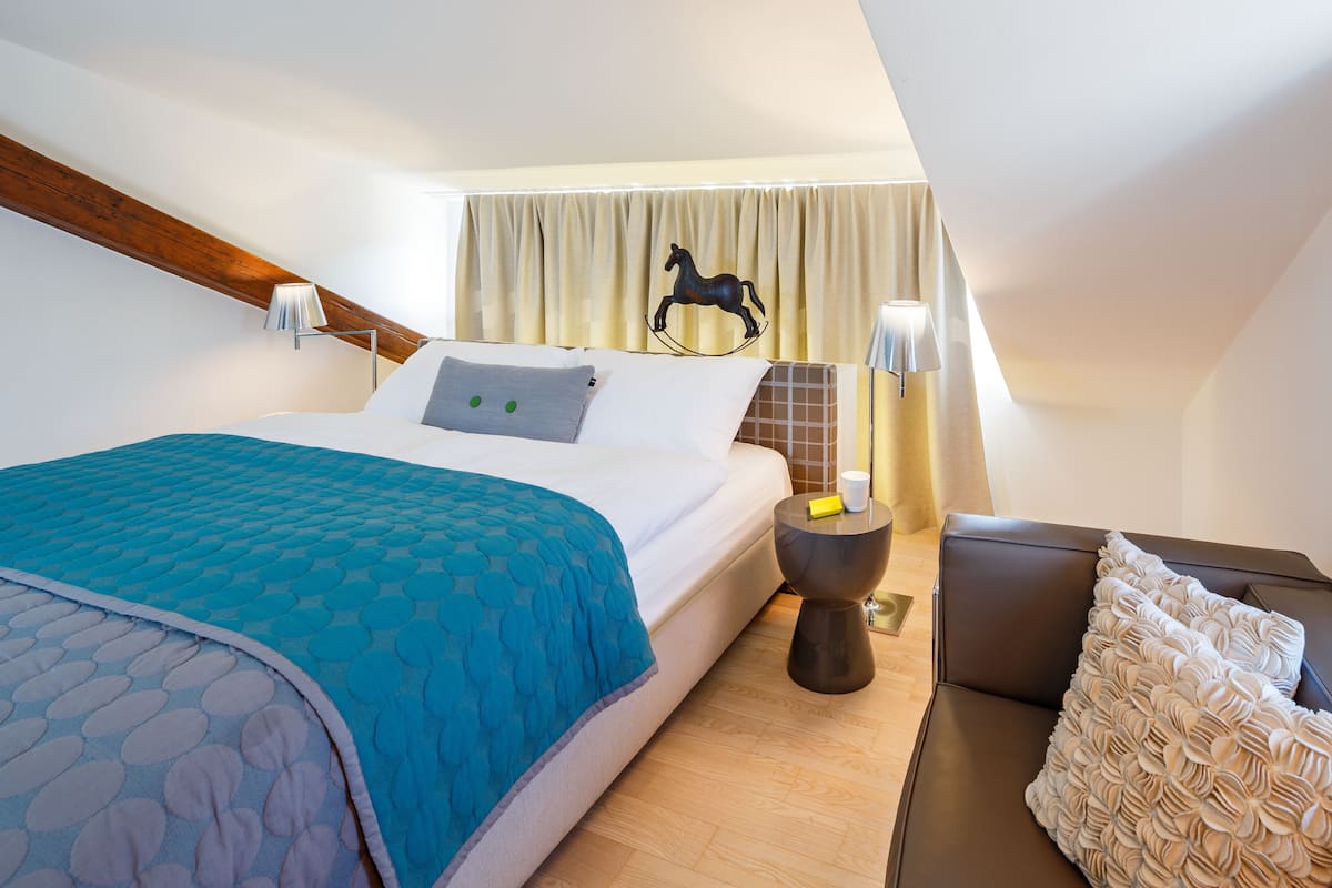 A hotel room with a bed, a nightstand, a lamp, a chair, and a curtain with a horse decoration.
