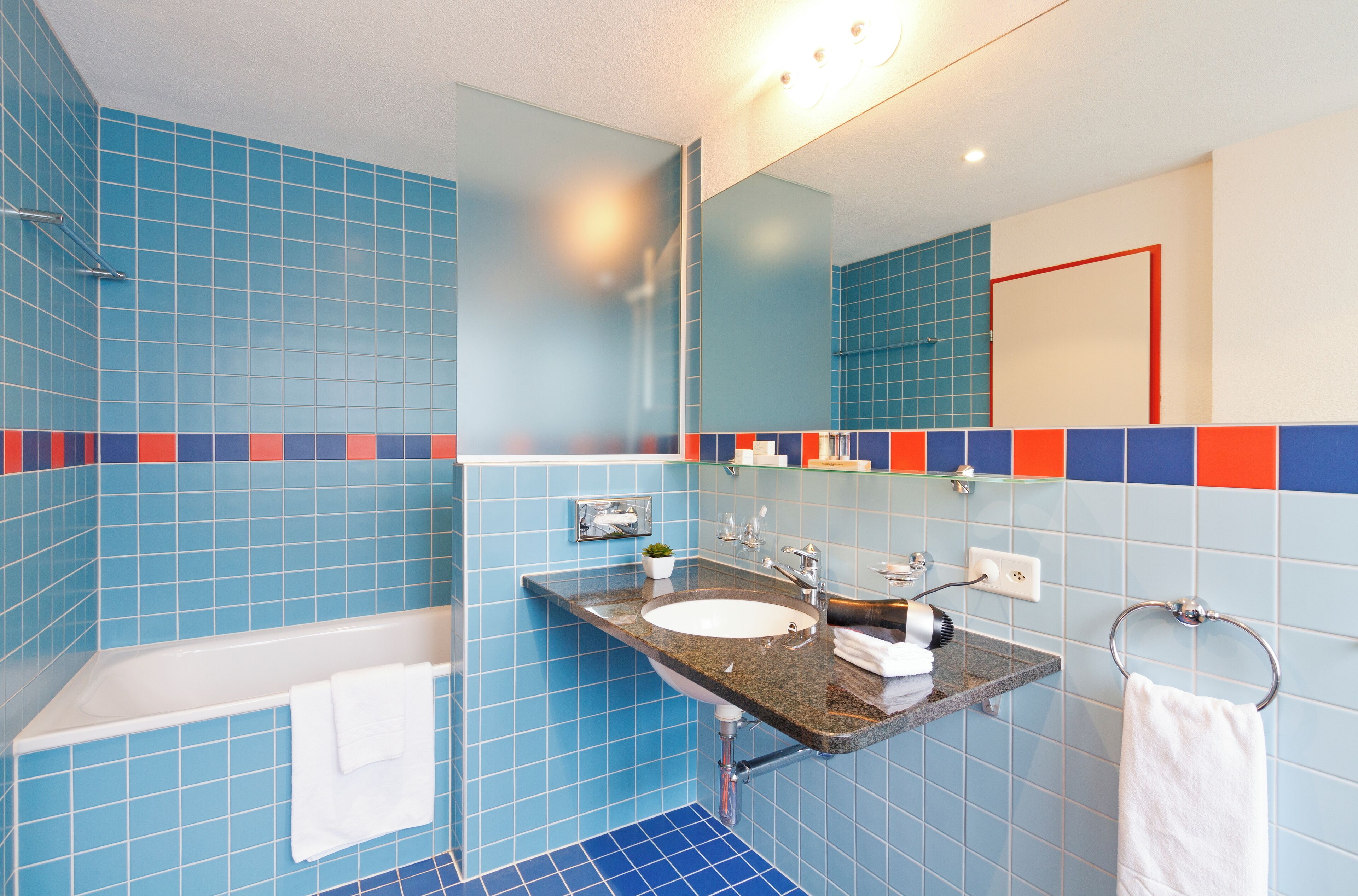 Une salle de bain avec des murs recouverts de carreaux bleus, une baignoire blanche, un évier en granit et un miroir au-dessus de l’évier.