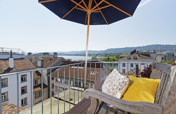 A balcony with a wooden railing, a large umbrella, and a view of a cityscape and water.