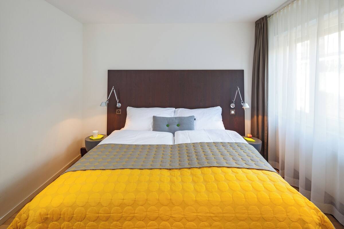 A neatly made bed with a yellow quilt, two bedside lamps, and a wooden headboard.