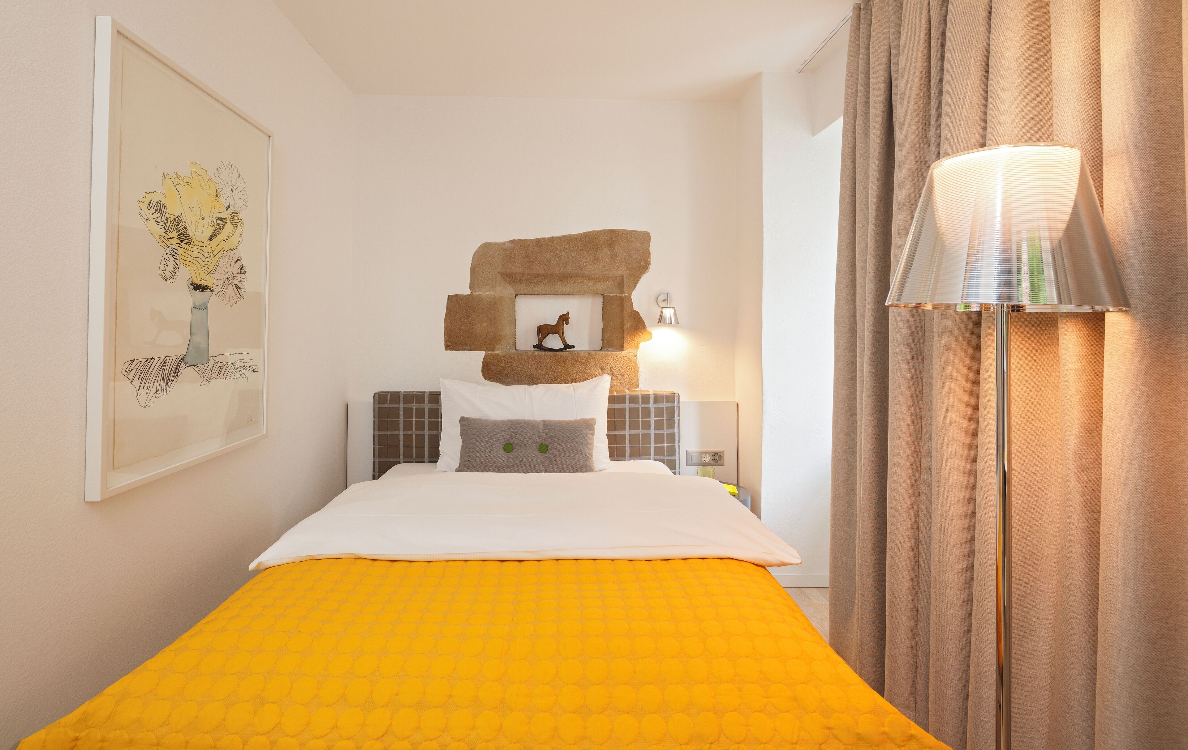 A hotel room with a bed, a headboard with a picture frame, a bedside lamp, and curtains.