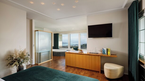A modern hotel room with a large bed, a wooden desk, a flat-screen TV, and a view of the sea. - UTO KULM - Top of Zurich (Zürich)