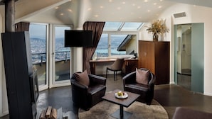 A modern living room with leather sofas, a coffee table, and a fireplace. There is a large window with a view of a cityscape. - Hotel UTO KULM car-free hideaway in Zurich (Zürich)