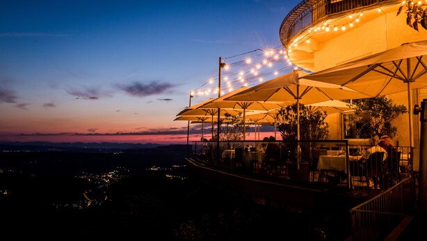 A restaurant with outdoor seating, a curved balcony, and string lights. - Hotel UTO KULM car-free hideaway in Zurich (Zürich)