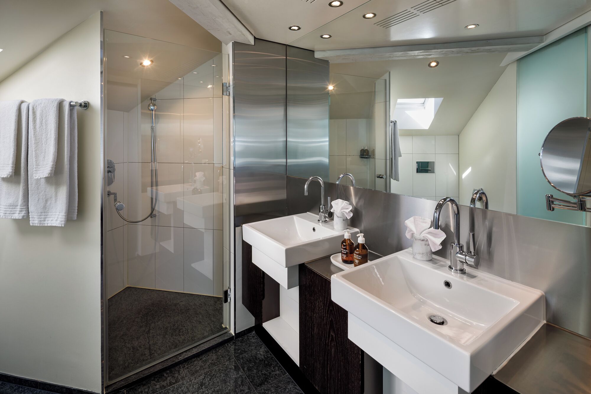 Un baño moderno con dos lavamanos, cabina de ducha de vidrio y un espejo grande.