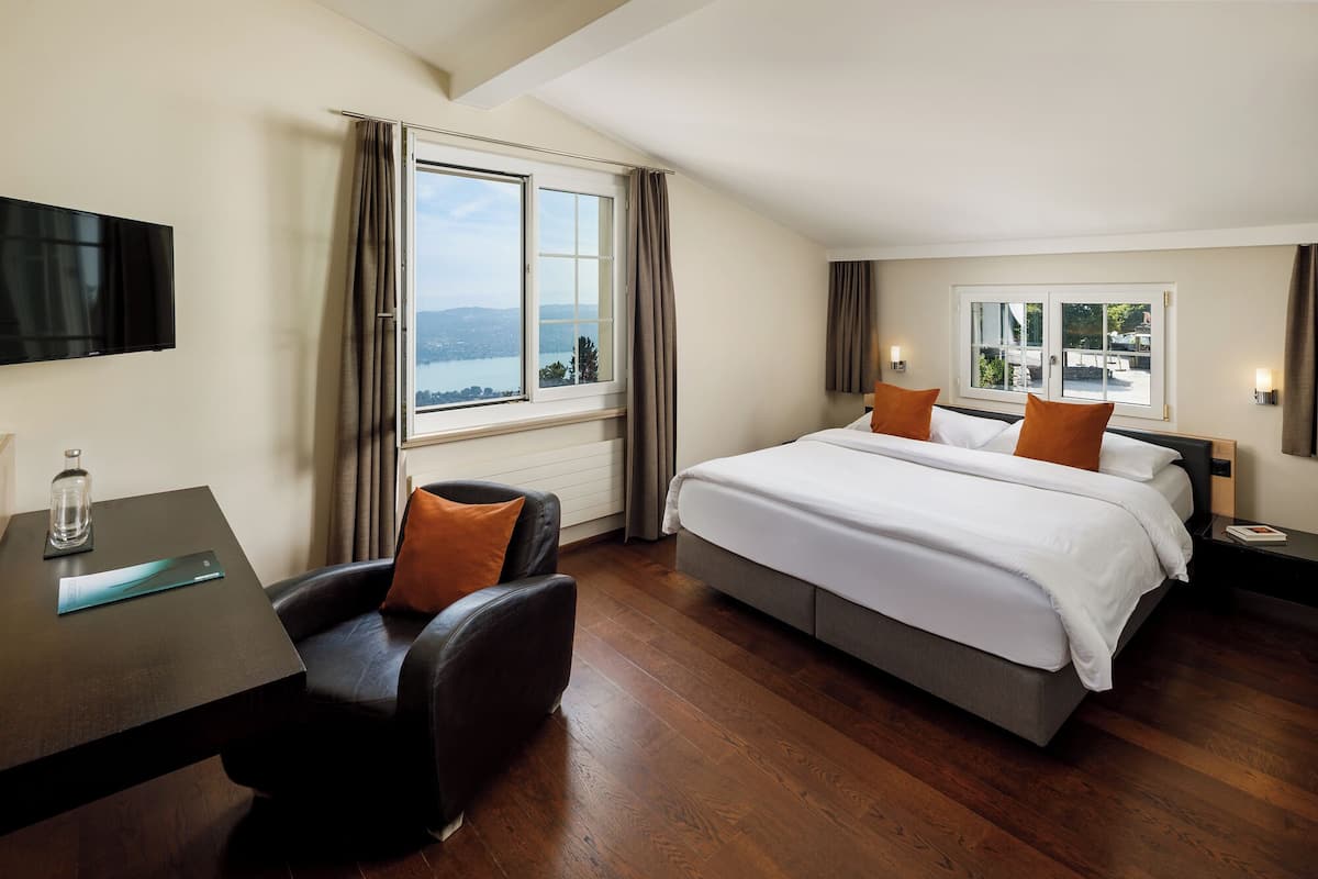Une chambre d’hôtel avec un lit, un bureau et une chaise. Il y a une fenêtre donnant sur un plan d’eau et des montagnes.