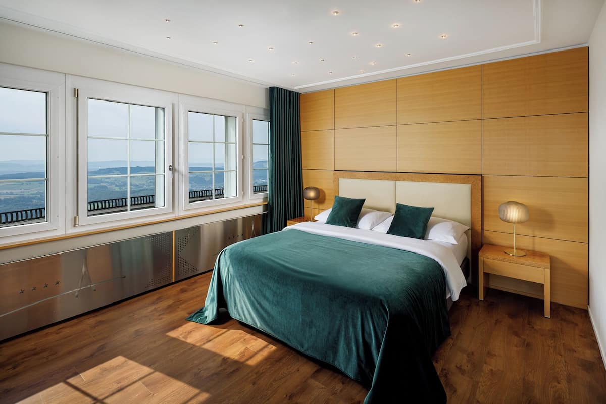 Une chambre moderne avec un grand lit, une vue dégagée grâce à de grandes fenêtres et un panneau mural en bois.