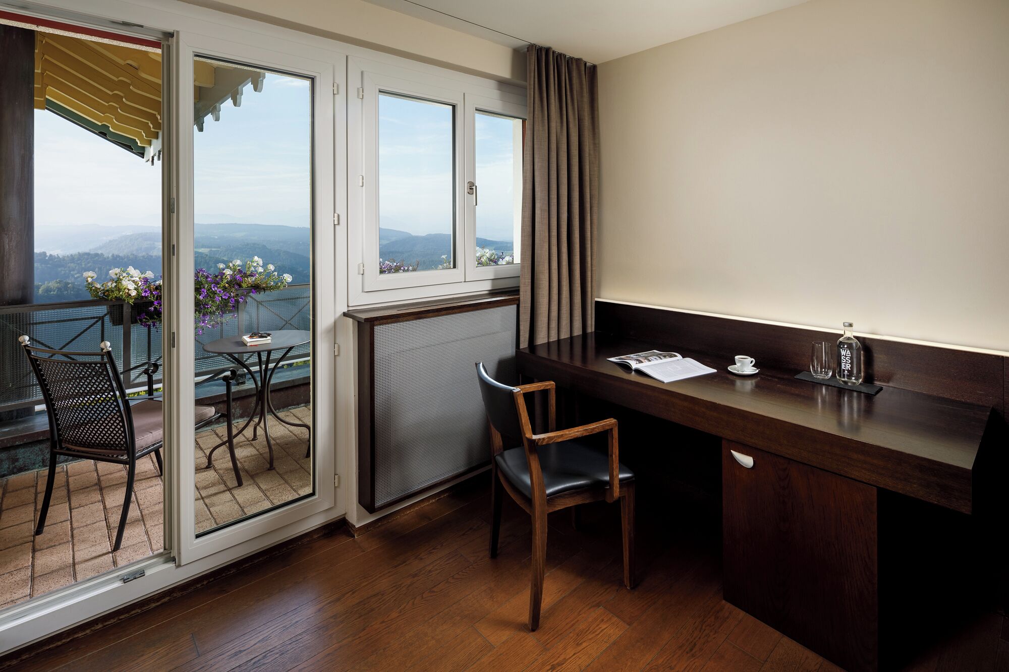 A balcony with a table and chairs, a view of the mountains, and a wooden desk with a chair.