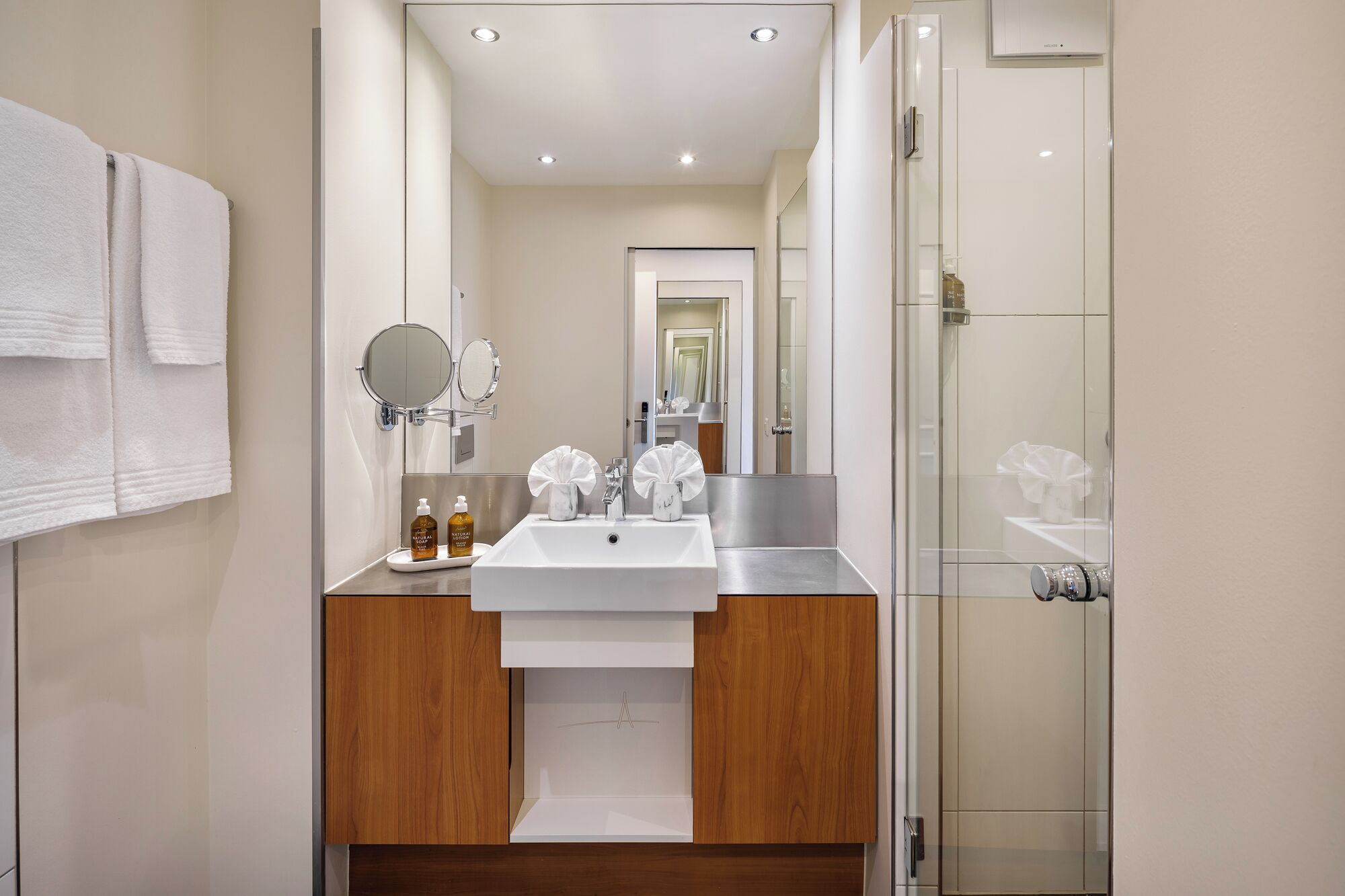 A modern bathroom with a white sink, wooden vanity, and a glass shower enclosure.