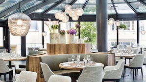A modern restaurant with round tables, cushioned seating, and hanging light fixtures. - Hotel UTO KULM car-free hideaway in Zurich (Zürich)