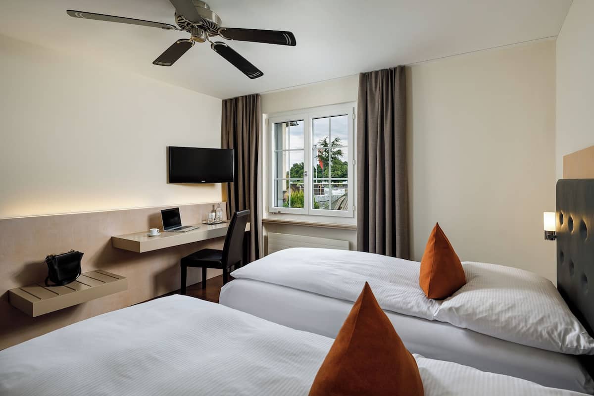 Une chambre d’hôtel avec deux lits, un bureau, une chaise, une télévision et un ventilateur de plafond.