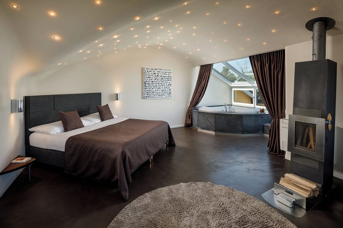 Une chambre moderne avec un grand lit, une cheminée, une fenêtre de toit et une vue sur un jacuzzi.