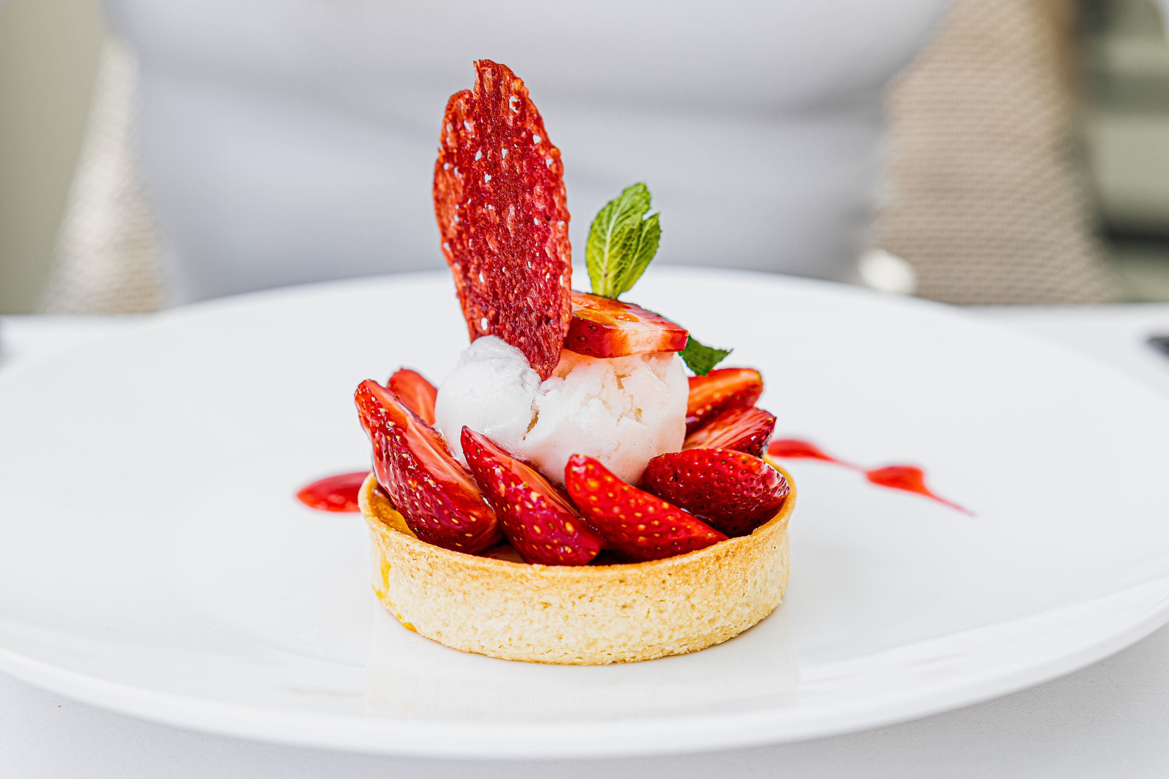 Un postre con fresas y menta sobre un plato blanco.