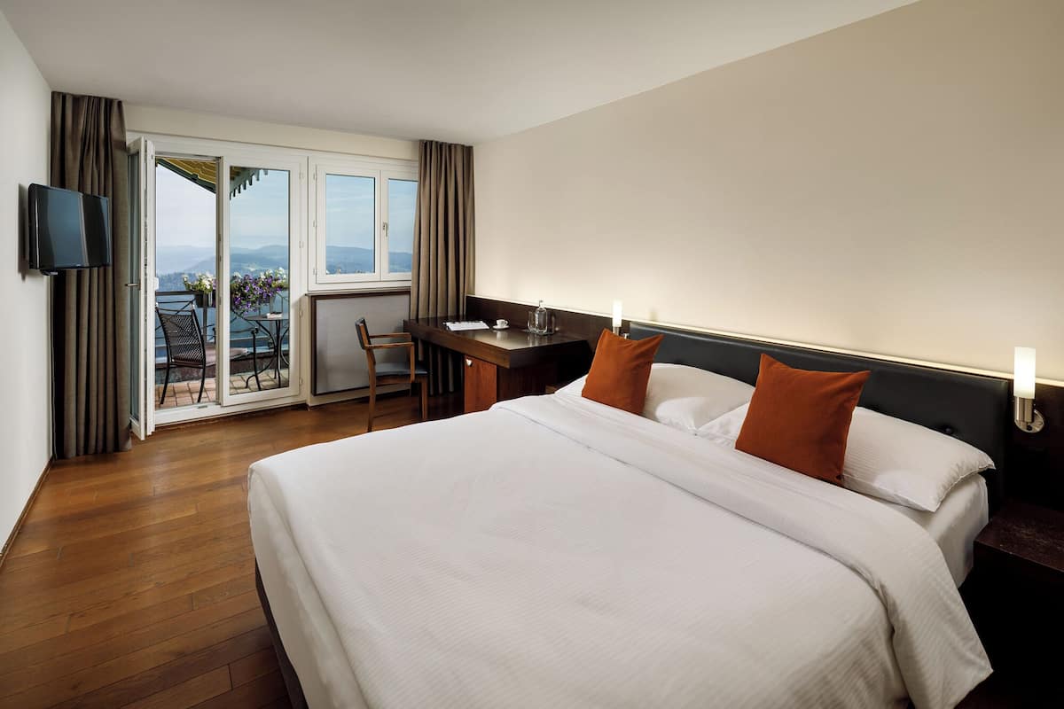 Une chambre d’hôtel avec un grand lit, un bureau, une chaise, une télévision et un balcon avec vue.