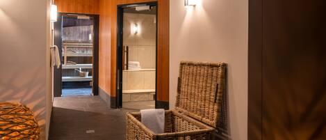 A hallway with a wicker chair, a wicker basket, and a view into a bathroom with a towel rack and a glass shower enclosure.