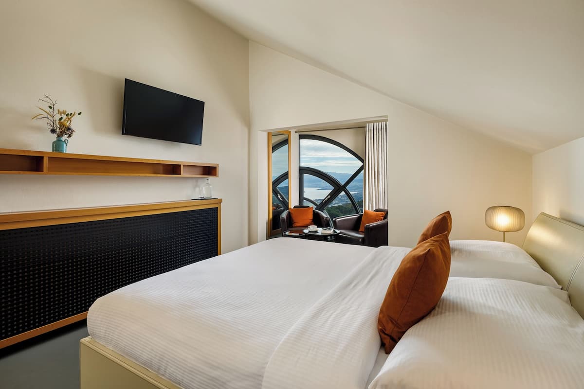 Une chambre d’hôtel avec un lit, un téléviseur fixé au mur, une fenêtre donnant sur un paysage agréable et un bureau avec une lampe.