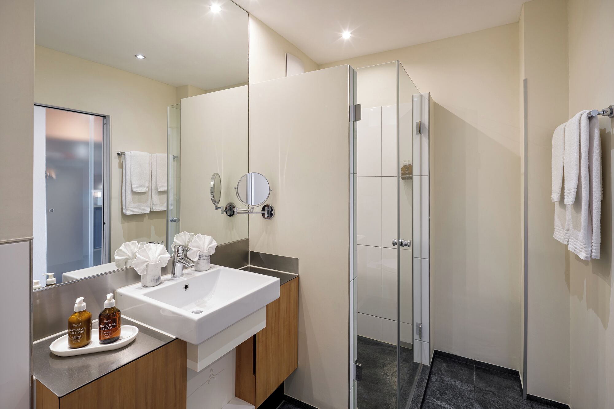 A modern bathroom with a glass shower enclosure, a white sink with a marble countertop, and a large mirror.