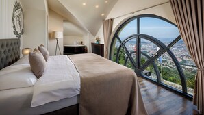 A bedroom with a large bed, a nightstand, a lamp, and a view of a city through a large window. - Hotel UTO KULM car-free hideaway in Zurich (Zürich)
