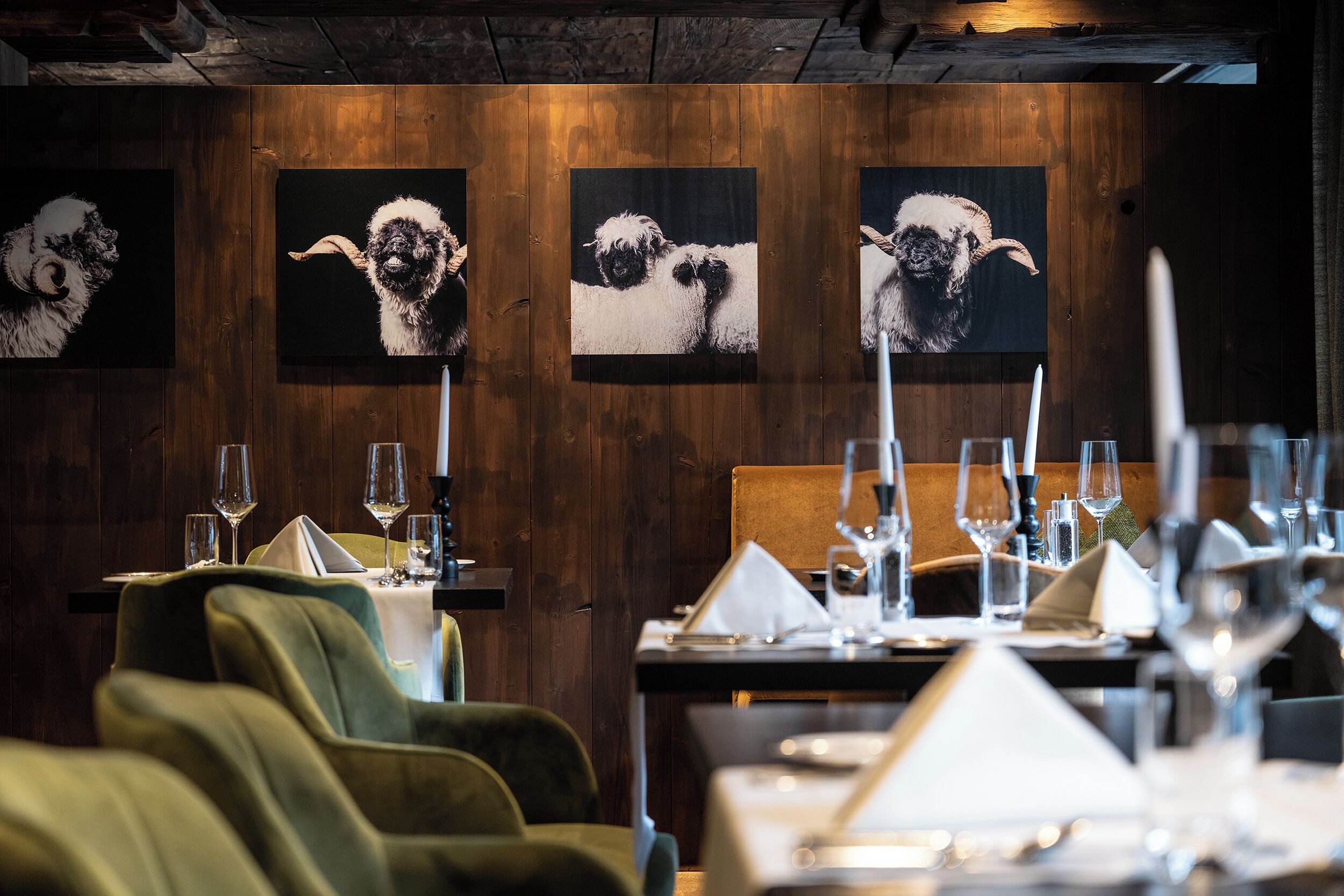 Ein Restaurantinneres mit Holzwänden, gedeckten Tischen mit Weingläsern und Kunstwerken, die Schafe zeigen.