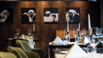 Ein Restaurantinneres mit Holzwänden, gedeckten Tischen mit Weingläsern und Kunstwerken, die Schafe zeigen.