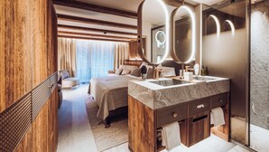 A modern hotel room with a large bed, a wooden vanity with a mirror, and a separate shower area. - Wellness Hotel Alpenhof (Zermatt)