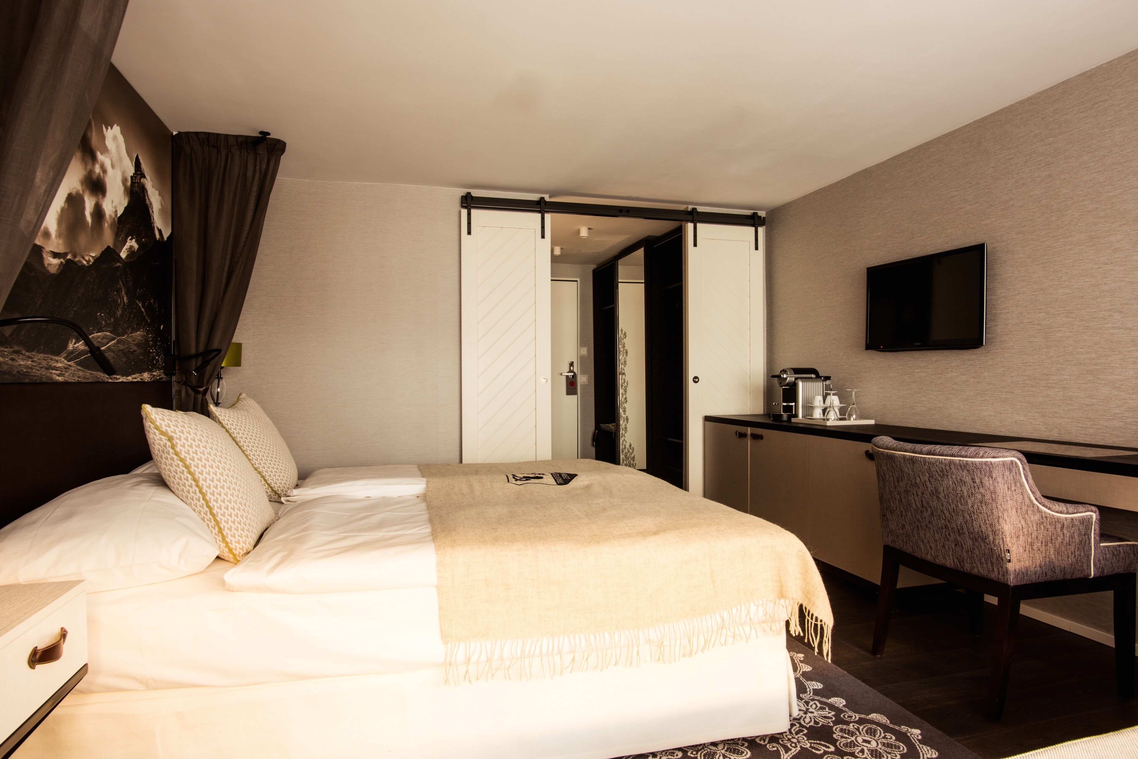 A hotel room with a bed, a desk, a chair, a television, and a wardrobe.