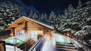 A log cabin with a sauna, a hot tub, and a pool, surrounded by snow-covered trees. - Wellness Hotel Alpenhof (Zermatt)
