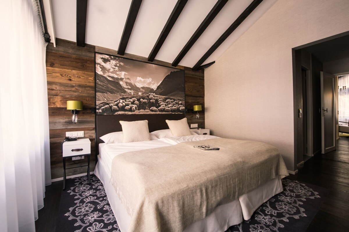 Une chambre à coucher avec un lit, des tables de chevet, une lampe fixée au mur et un grand tableau encadré.