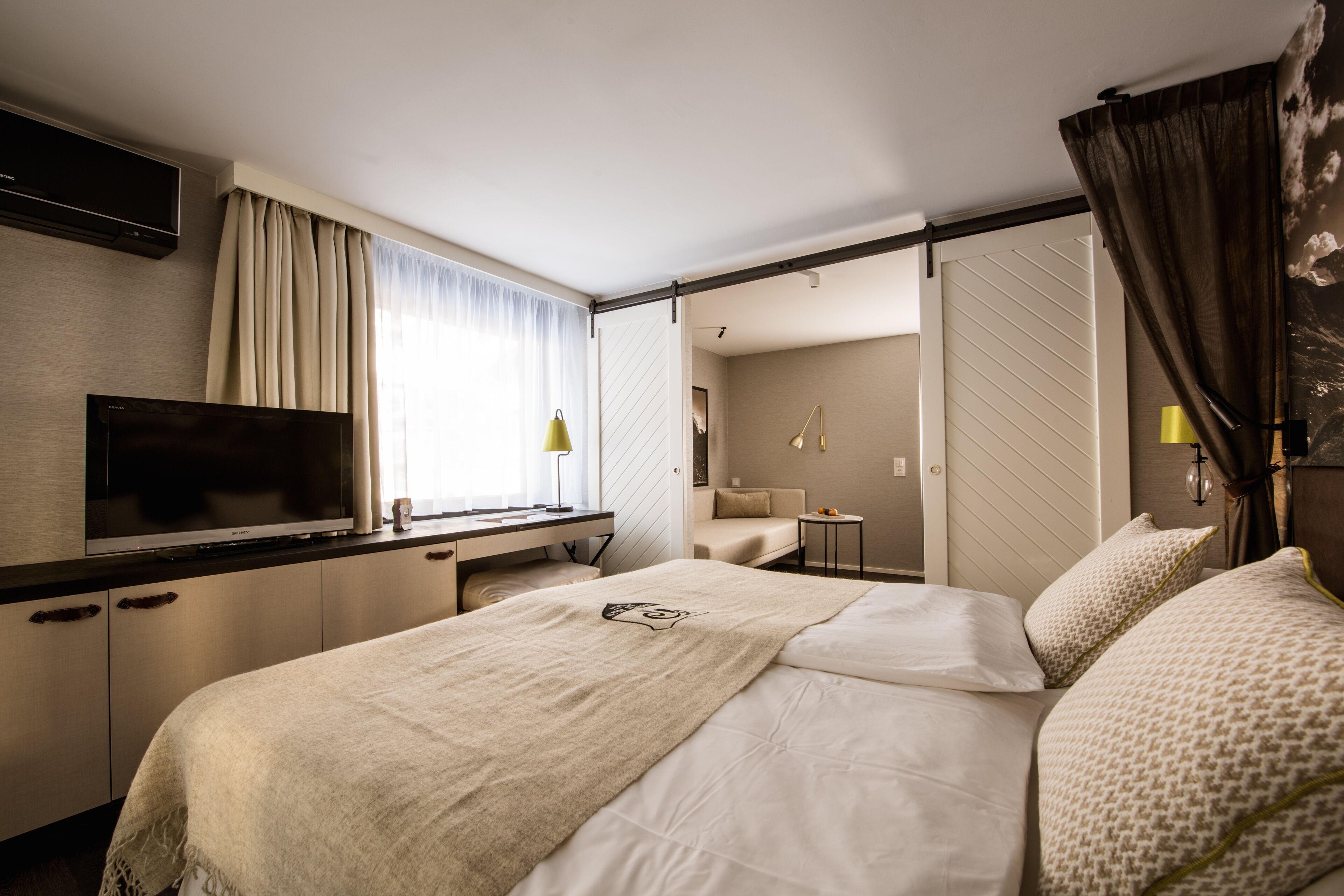 A hotel room with a bed, a desk, a TV, and a bathroom visible through an open door.
