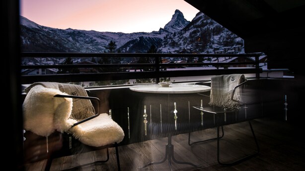 A balcony with two chairs and a table, overlooking a snowy mountain landscape. - Wellness Hotel Alpenhof (Zermatt)