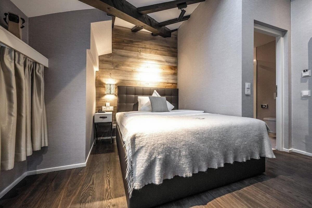 Un dormitorio con cama, mesita de noche, lámpara y una pared de madera decorativa.