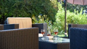An outdoor seating area with wicker furniture and a glass table, featuring two glasses of red wine and a vase. - Hôtel de l'Aigle (Val-de-Travers)