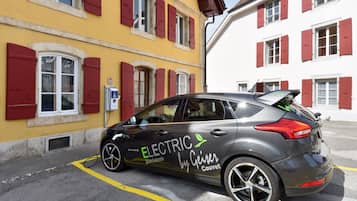 Ein graues Elektroauto vor einem gelben Gebäude mit roten Fensterläden.